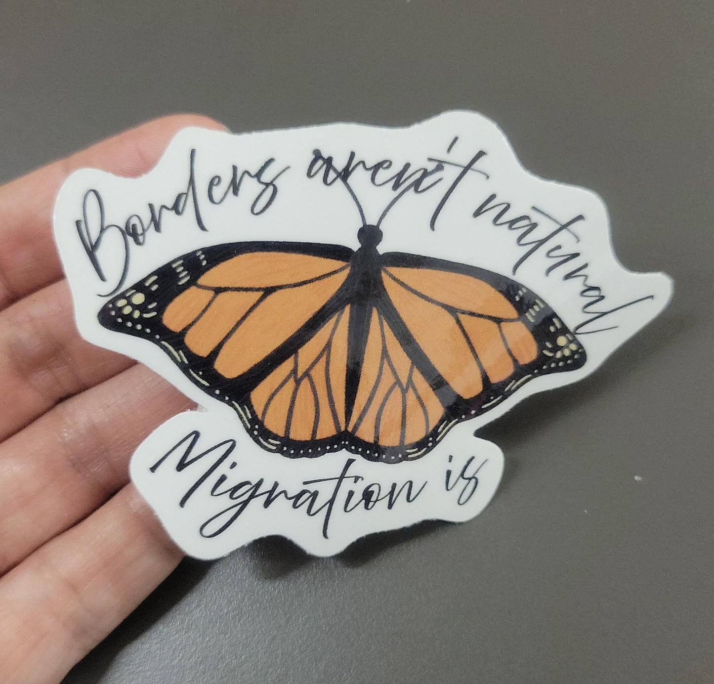 Pro-immigration sticker with a monarch butterfly design and text that says Borders aren't natural, migration is.