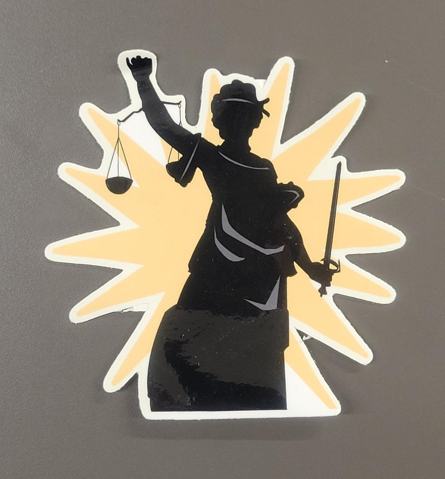 Sticker of a silhouette holding a sword and scales on a gray background