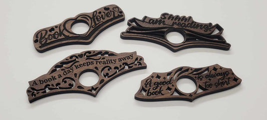 Made from premium walnut wood, the Laser Cut Wood Book Holder by InkBird Print Studio LLC. Photo shows four wooden thumb bookmarks that every book lover will cherish. With engraved phrases such as A book a day keeps reality away! and Shhh! I am reading!, they serve as both practical tools and meaningful gifts for avid readers.
