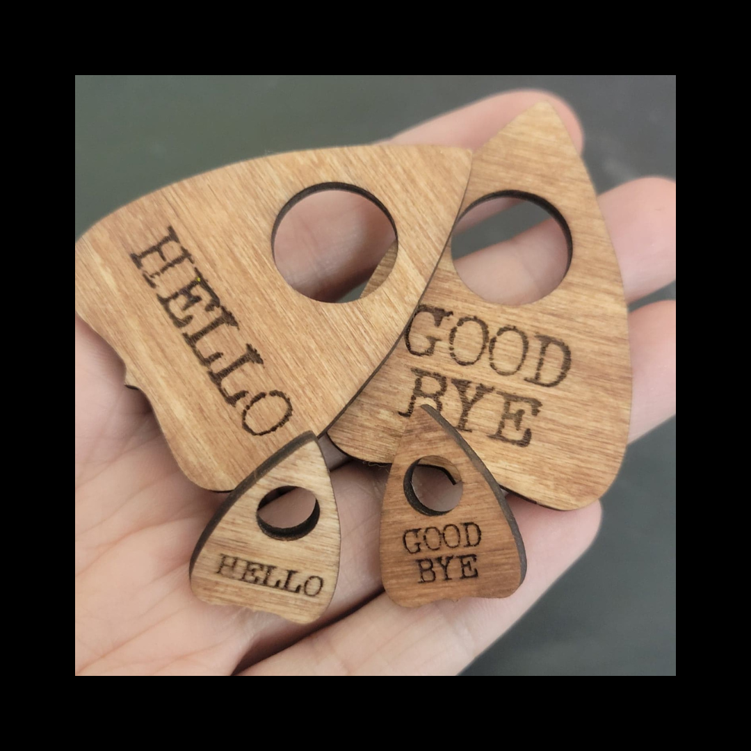 Hand holding four laser-cut wood Ouija planchette pins by InkBird Print Studio: 2 large, 2 small, engraved HELLO or GOOD BYE.