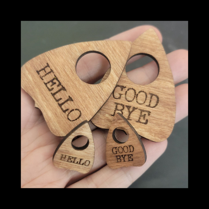 Hand holding four laser-cut wood Ouija planchette pins by InkBird Print Studio: 2 large, 2 small, engraved HELLO or GOOD BYE.