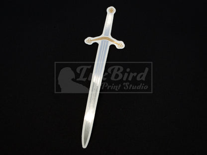 Vinyl sticker of a Scottish Claymore sword in silver and gold foil on black; durable adhesive, medieval-inspired, unique detailing.