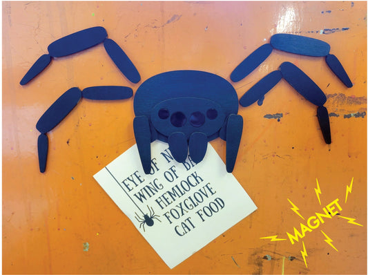 Black laser-etched wood spider magnet with movable legs, yellow lightning bolts to indicate magnetism, and “MAGNET” text in the corner.